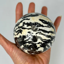 Load image into Gallery viewer, Hand holding a zebra-striped shaped and polished sphere stone against a plain background
